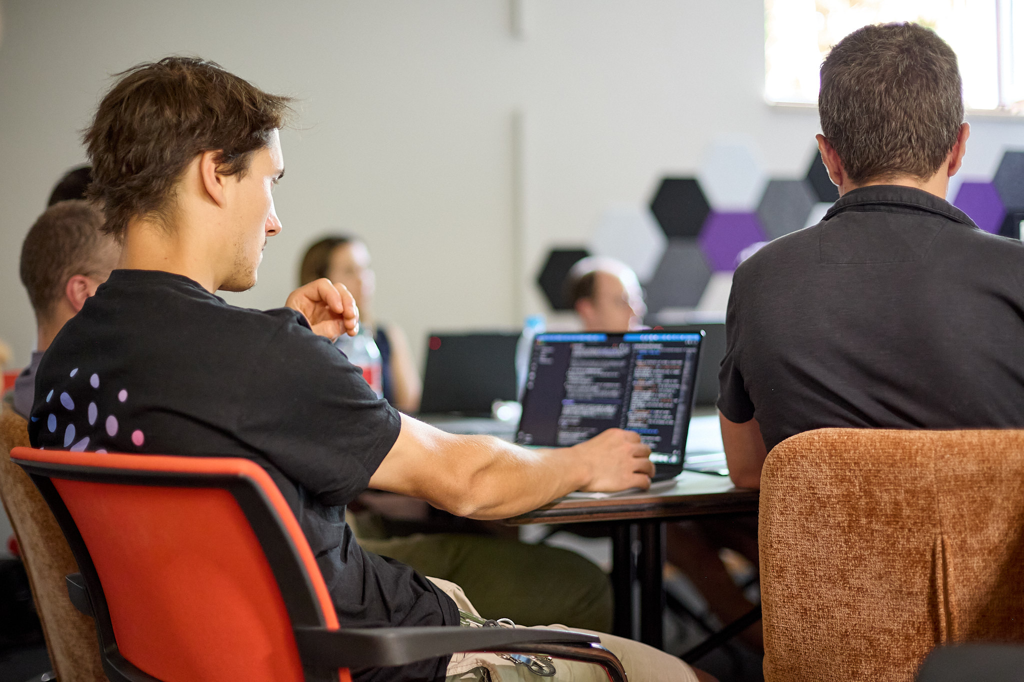 Two participants work at their laptops during the planqc workshop, one of them typing into an editor full of code